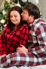 in love and happy man and woman in red checkered pajamas at the Christmas tree.