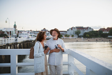 Fototapeta na wymiar Happy senior couple tourist having fun on walk outdoors on pier by sea, summer holiday.