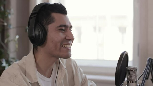 Man speaker talking and smiling, sitting at table in front of microphone in modern studio epspb. Closeup view of young male presenter speaks something and looks with smile, records business podcast