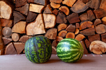 Striped watermelons lie in front of chopped wood..