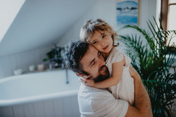 Mature father hugging with small daughter indoors in bathroom at home.