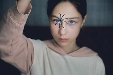 Portrait of a girl in a dark room close-up in front of her face holds a spider hanging on a web.