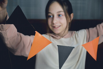 Happy girl holding in front of her a cut out garland of orange and black triangles in the hallowne style.