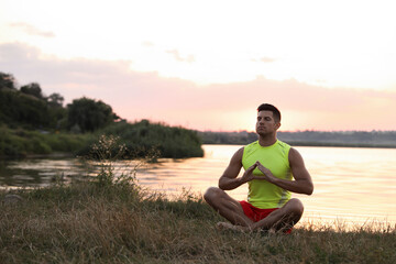 Naklejka na ściany i meble Man meditating near river in twilight. Space for text