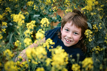 Boy with mullet playing in vibrant yellow canola field in full bloom