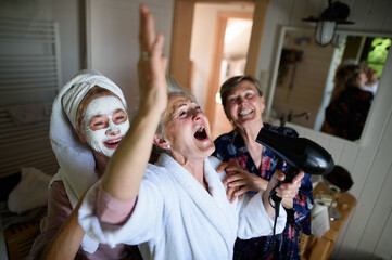 Happy senior women friends in bathrobes having fun indoors at home, selfcare concept.