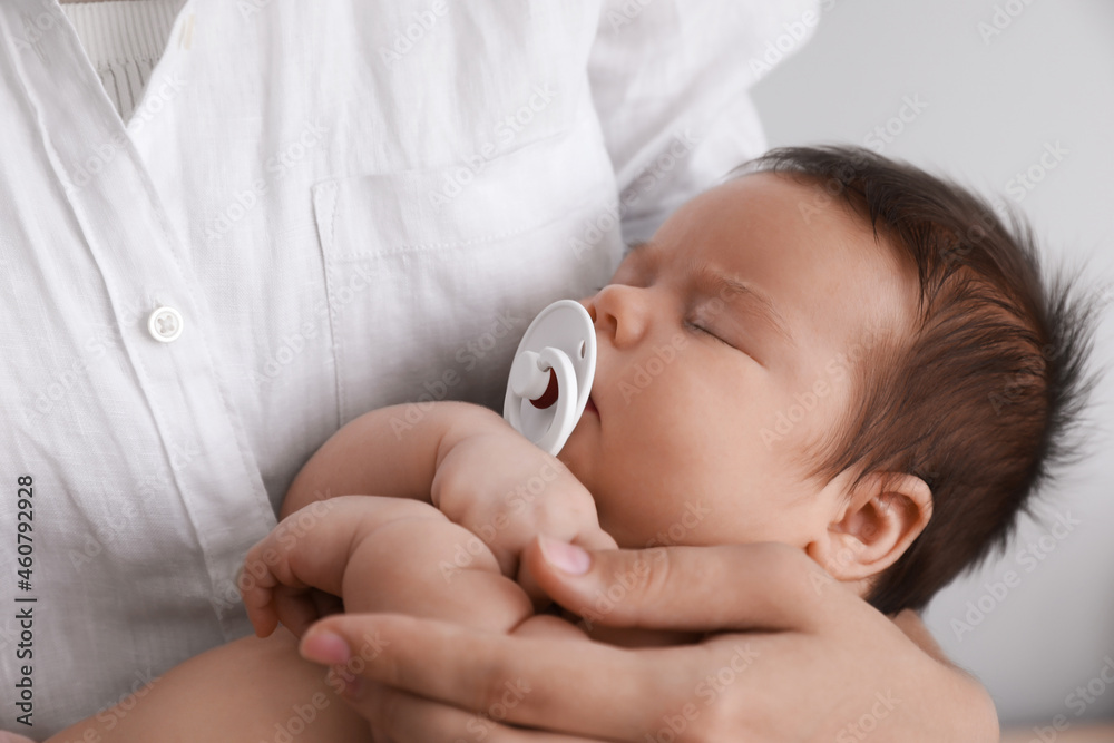 Canvas Prints Mother holding her cute little baby with pacifier on light background, closeup