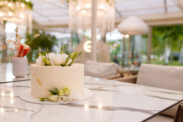 Soft focused shot of beautiful white wedding or birthday cake with roses flowers on marble table, restaurant background. Festive event sweet bakery