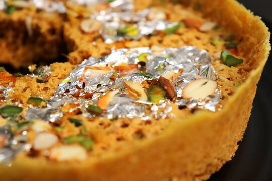 Rajasthani Ghevar. Ghewar is an Indian crunchy sweet dish made using refined flour, sugar, and ghee. Garnished with silver foil and dry fruits. Over dark background with copy space.