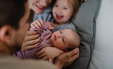 Happy young family with newborn baby and little girl enjoying time together at home. - obrazy, fototapety, plakaty