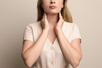 Young woman doing thyroid self examination on beige background, closeup