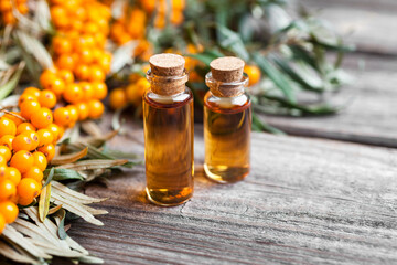 Natural oil of sea buckthorn (Hippophae) in glass bottle with branch of fresh, juicy ripe yellow berries with green leaves on a wooden background