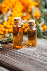 Natural oil of sea buckthorn (Hippophae) in glass bottle with branch of fresh, juicy ripe yellow berries with green leaves on a wooden background