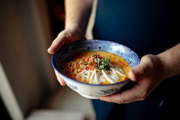 Chef holding a bowl of japanese curry chicken ramen with tomatoes