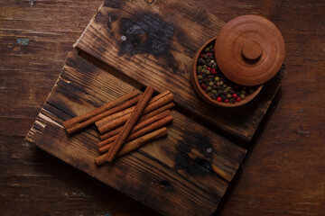 Pot of aromatic pepper set, allspice peas, cinnamon sticks on wooden kitchen board on country table. Flavourings, seasonings