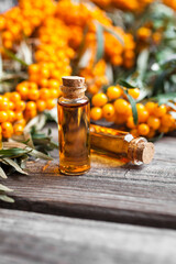 Natural oil of sea buckthorn (Hippophae) in glass bottle with branch of fresh, juicy ripe yellow berries with green leaves on a wooden background