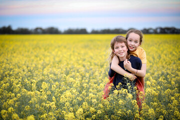 Fototapeta premium Brother and sister playing together in vibrant canola field in full bloom