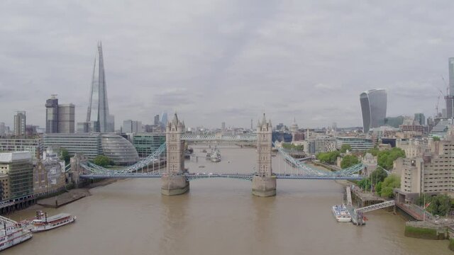 Aerial drone wide establishing shot over the River Thames of Tower Bridge and The Shard looking over London skyline on a bright, grey cloudy day, with traffic crossing the bridge