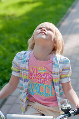 Cute blonde caucasian girl riding bicycle and looking up at the park. Summer vacation happy childhood