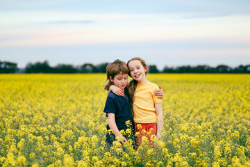 Fototapeta premium Brother and sister playing together in vibrant canola field in full bloom