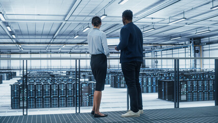 Data Center Female System Administrator and Male IT Specialist Talk, Use Laptop. Information Technology Engineers work on Cyber Security Network Protection in Cloud Computing Server Farm.