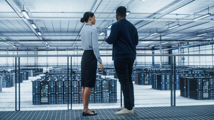 Data Center Female System Administrator and Male IT Specialist Talk, Use Laptop. Information Technology Engineers work on Cyber Security Network Protection in Cloud Computing Server Farm.