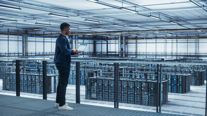 Data Center Engineer Using Laptop Computer. Server Farm Cloud Computing Specialist Facility with African American Male System Administrator Working with Data Protection Network for Cyber Security.