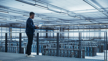 Data Center Engineer Using Laptop Computer. Server Farm Cloud Computing Specialist Facility with African American Male System Administrator Working with Data Protection Network for Cyber Security.