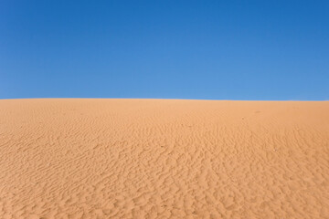 Naklejka premium Ripple sand dunes and blue sky background. Desert landscape, sandy waves. Nature.