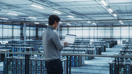 Data Center Engineer Using Laptop Computer. Server Farm Cloud Computing Specialist Facility with...
