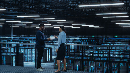 Data Center Female System Administrator and Male IT Specialist Talk, Use Laptop Computer. Information Technology Engineers work on Cyber Security Network Protection in Cloud Computing Server Farm.