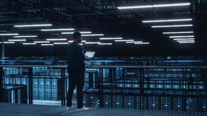 Data Center Engineer Using Laptop Computer. Server Farm Cloud Computing Specialist Facility with...