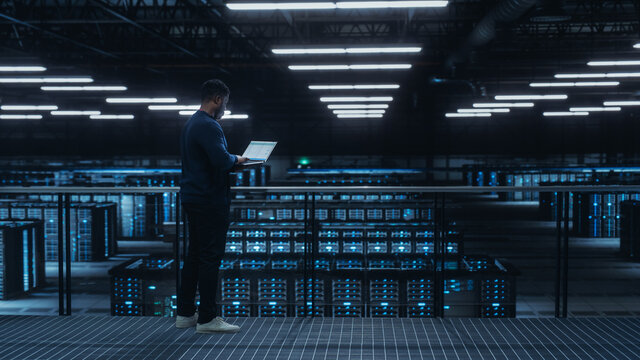 Data Center Engineer Using Laptop Computer. Server Farm Cloud Computing Specialist Facility with African American Male System Administrator Working with Data Protection Network for Cyber Security. - Powered by Adobe