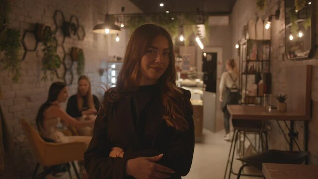 A spectacular young girl in black clothes is standing in the lobby of a stylish cafe and straightening her long hair. Slow motion