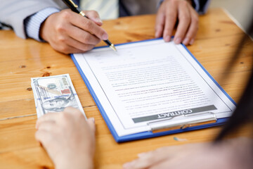 Close up of Businessman puts signature on a contract at the business meeting and passing money after negotiations with business partners.