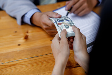 Close up of Businessman puts signature on a contract at the business meeting and passing money after negotiations with business partners.
