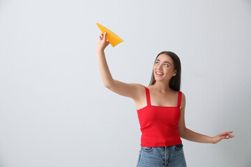 Beautiful young woman playing with paper plane on light grey background. Space for text