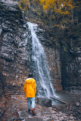 woman in yellow raincoat at autumn waterfall