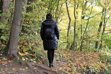 Woman in black leather coat enjoying the nature walking in autumn park. Concept of environment, vacation and travel