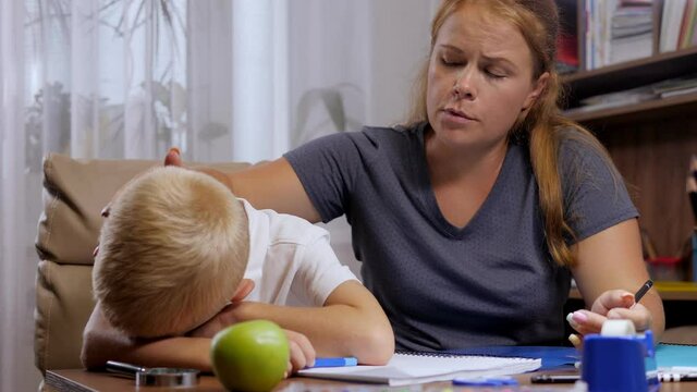 A little boy cries when doing homework at home, an angry mother shouts at the child. They are sitting at a desk with school supplies. Problems of children and parents.