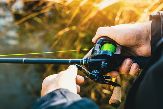 fishing rod with multiplier reel and green braided line in angler hands. closeup