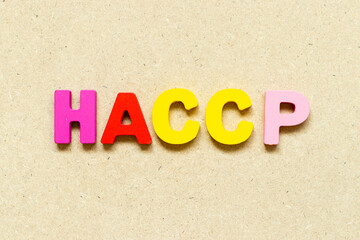 Color alphabet letter with word HACCP (Hazard Analysis Critical Control Points) on wood background