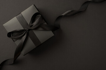 Top view photo of black giftbox with black satin ribbon bow on isolated black background with copyspace