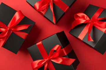 Top view photo of levitating black gift boxes with red ribbon bow on isolated red background