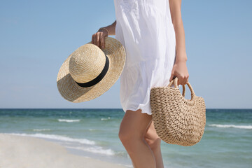 Woman with beach bag and straw hat near sea, closeup