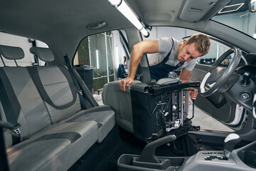 Naklejka premium Worker removes car seat for interior cleaning at auto service closeup