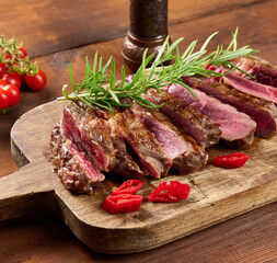 roasted piece of beef ribeye cut into pieces on a vintage brown chopping board, rare doneness. Delicious steak