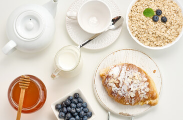 Obraz na płótnie Canvas Raw oatmeal in white ceramic plate, blueberry, honey on white table, breakfast. top view
