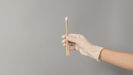 Cotton sticks for swab test in hand with white medical gloves on grey background.
