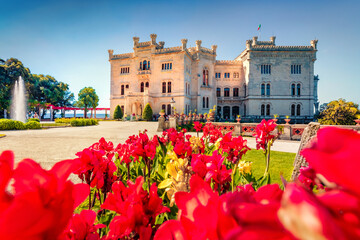 Bright summer view of Miramare Castle with blooming red tulip flowers on foreground. Sunny morning scene of Italy, Europe. Traveling concept background..